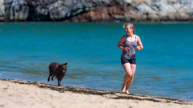 Woman running with a dog on Ocean Path in Bar Harbor - a beautiful dog friendly beach in Maine, USA